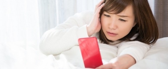 スマホを見て面倒な表情をする女性のイメージ