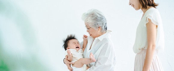 親に子どもを預ける母親　孫を抱く祖母　イメージ画像